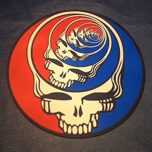 May include: A round, blue and red patch with a swirling, psychedelic image of a skull. The skull is yellow and has a white outline.
