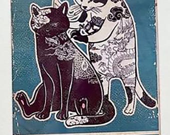 May include: A rectangular metal sign with a teal background featuring a black cat sitting while being tattooed by a white and black cat. The sign displays the text CATS & TATS in a bold, light-colored font at the bottom, with visible wear and distressed edges.