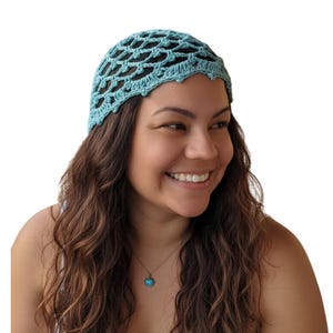 May include: A light blue crochet head wrap with an open, net-like design. The head wrap is worn by a person with long, wavy brown hair. A gold necklace with a turquoise pendant is also visible.