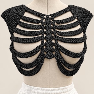 May include: A black crochet top featuring a rib cage design with a central vertical column and horizontal curved bands extending outward. The garment has short cap sleeves and a textured, knotted yarn construction that forms an openwork pattern.