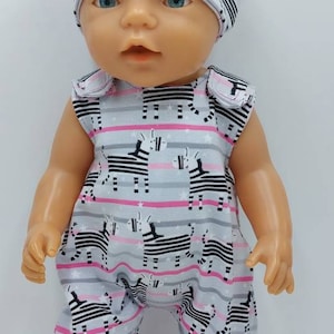 以下が含まれることがあります： グレーとピンクのストライプのジャンプスーツを着た人形。黒と白のシマウマ柄です。人形はグレーとピンクのシマウマ柄のヘッドバンドも着用しています。