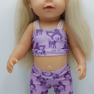 May include: A doll wearing a purple and gold two-piece outfit with a deer print. The doll has blonde hair and blue eyes.