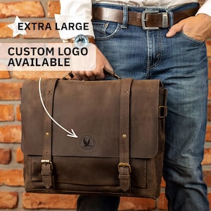 May include: A brown leather messenger bag with a flap closure, adjustable straps, and brass-colored buckles. The bag features a circular logo and the text "EXTRA LARGE CUSTOM LOGO AVAILABLE". The bag is held by a person wearing blue jeans and a brown belt.