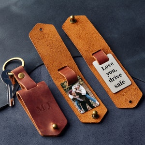 May include: A brown leather keychain with a silver tag that says "Love you, drive safe". The keychain also has a photo insert and a personalised initial tag that says "MJ".