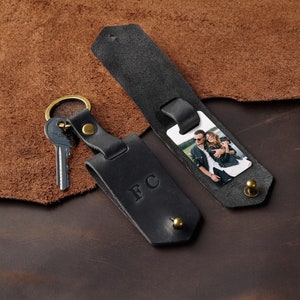 May include: Black leather keychain with a photo insert and a key ring. The photo insert shows a couple smiling. The keychain has the initials "FC" embossed on it.