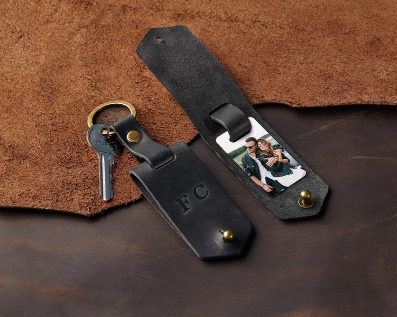 May include: Black leather keychain with a photo insert and a key ring. The photo insert shows a couple smiling. The keychain has the initials "FC" embossed on it.