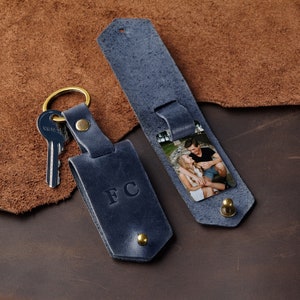 May include: A blue leather keyring with a photo insert and the initials "FC" embossed on the front. The keyring has a brass key ring and a brass snap closure.
