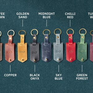 May include: Ten leather keyrings with different coloured leather and metal rings. Each keyring has the word "DAD" embossed on the leather. The colours are coffee brown, golden sand, midnight blue, chilli red, tuscan wine, copper, black onyx, sky blue, green forest.