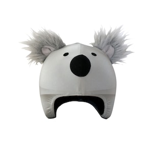 Puede incluir: Un sombrero gris claro con temática de koala con una nariz negra y ojos negros pequeños. El sombrero tiene orejas grises esponjosas y una correa para la barbilla. El sombrero está diseñado para cubrir la cabeza y las orejas.
