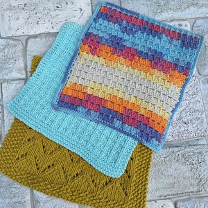May include: Three crocheted dishcloths in different colours and patterns. One is a light blue dishcloth with a simple stitch pattern, another is a yellow, orange, and pink dishcloth with a textured stitch pattern, and the third is a mustard yellow dishcloth with a lacy stitch pattern.