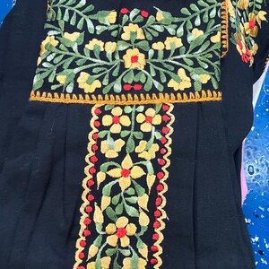 May include: Black embroidered top with floral designs. The embroidery features yellow flowers, green leaves, and red accents. The top has a square neckline and short sleeves, with a decorative trim.
