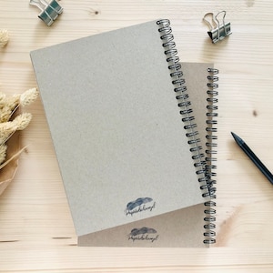 Puede incluir: Dos cuadernos de espiral marrones con el texto "papierdeengel" impreso en la portada. Los cuadernos est&aacute;n sobre una superficie de madera clara con un l&aacute;piz y clips.