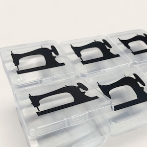 May include: Clear plastic storage containers with black sewing machine silhouettes on the lids. The containers are arranged in a grid pattern, with the lids slightly ajar, revealing the empty interiors. The background is plain white.