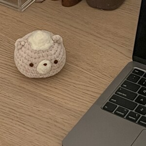 Peut inclure: Un ours en crochet rose clair avec une touffe blanche et des yeux bruns est pos&eacute; sur un bureau en bois. Un ordinateur portable est &agrave; c&ocirc;t&eacute; de l'ours. Th&egrave;me : artisanat et d&eacute;coration d'int&eacute;rieur.