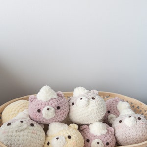 Peut inclure: Un panier en osier rempli de jouets ours en crochet faits &agrave; la main. Les ours sont de diff&eacute;rentes couleurs pastel, dont le blanc, le rose et le jaune. Chaque ours a une petite touffe blanche et des yeux brun fonc&eacute;.