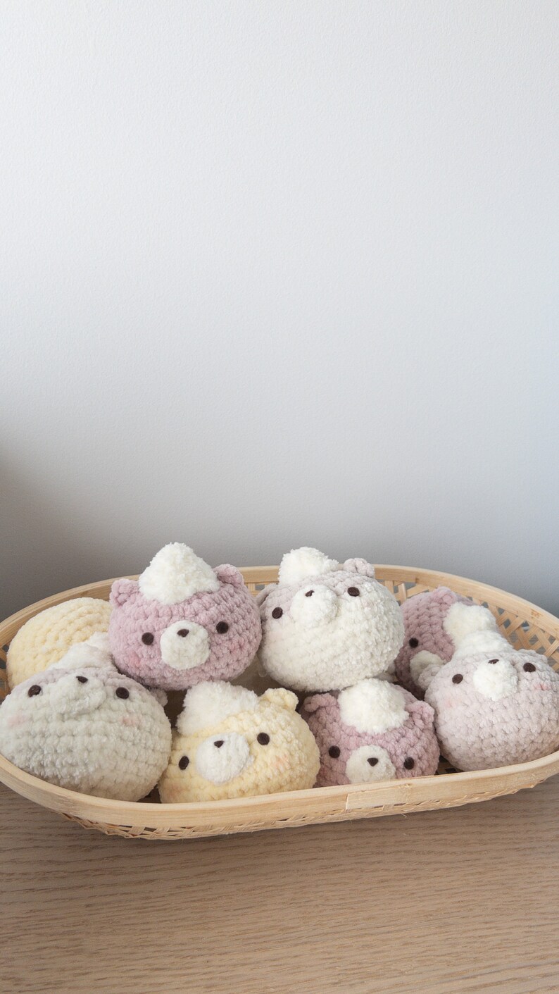 Peut inclure: Un panier en osier rempli de jouets ours en crochet faits &agrave; la main. Les ours sont de diff&eacute;rentes couleurs pastel, dont le blanc, le rose et le jaune. Chaque ours a une petite touffe blanche et des yeux brun fonc&eacute;.