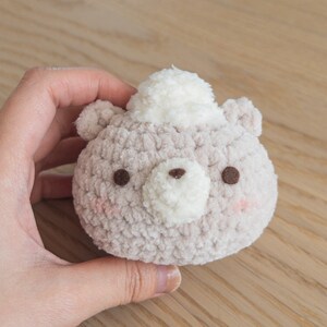 Peut inclure: Un jouet en forme d'ours rond et moelleux, de couleur beige clair, avec un chapeau pompon blanc. L'ours a des yeux bruns et un museau blanc. Des joues roses accentuent le tout, cr&eacute;ant une esth&eacute;tique mignonne et faite &agrave; la main.