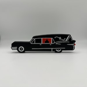 May include: A black toy car shaped like a hearse with red curtains in the back window. The car has a skull and crossbones design on the side.