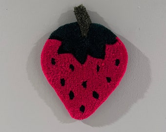 May include: A red and green felt strawberry with black seeds. The strawberry is a wall hanging.