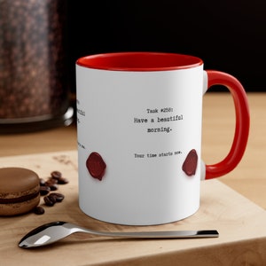 May include: White ceramic mug with a red rim and handle. The mug has a typewriter font design that reads "Task #258: Have a beautiful morning. Your time starts now." with two red wax seals on the bottom.