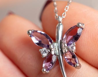 May include: A silver-toned necklace featuring a butterfly-shaped pendant. The pendant is crafted with four marquise-cut purple amethyst gemstones for the wings, accented by two small clear round-cut stones, all set in a polished silver metal frame.