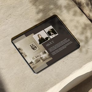 Op de afbeelding: Een tabletcomputer die een website weergeeft met een donkere achtergrond en witte tekst. De tekst luidt "ABOUT" en bevat informatie over de website. De website bevat ook afbeeldingen van een vrouw en een kamer met meubels.