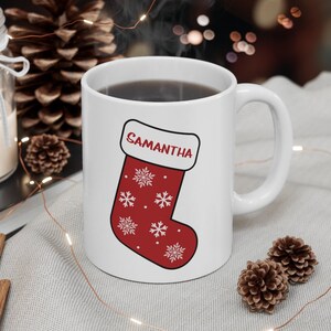 May include: White ceramic mug with a red and white Christmas stocking design. The stocking has snowflakes and the name "Samantha" on it.