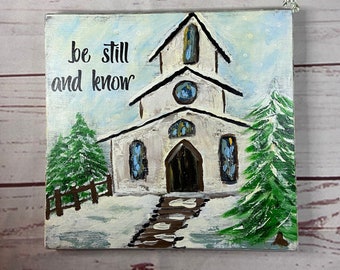 May include: A white church with a blue door and windows, surrounded by snow and pine trees. The text "be still and know" is written in black on a white background.
