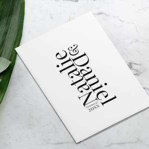 May include: White wedding guest book with black text that reads "Natalie & Daniel" and "October 17, 20XX".