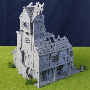 May include: A grey, miniature, ruined building with a weathered appearance. The model features a multi-storey design with a damaged roof, exposed beams, and detailed architectural elements. The building is set on a green surface.