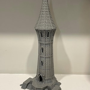 以下が含まれることがあります： 尖塔の屋根と石造りの土台を持つ、グレーの3Dプリントされた塔。塔には窓と入り口があります。塔は白い表面の上に置かれています。