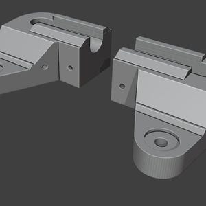 May include: Two gray, geometric, mechanical components. Each piece has a rounded base with a circular hole, a rectangular top with a groove, and several smaller holes. The pieces are designed to fit together.