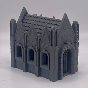 Puede incluir: Un modelo de iglesia gótica pequeña de color gris, impreso en 3D, con un techo puntiagudo, ventanas arqueadas y una puerta con una escalera en el interior.