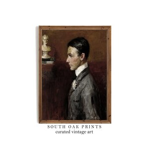 以下が含まれることがあります： グレーのスーツに白い襟を着た若い男性の油絵が額装されています。絵は濃い茶色の背景に描かれており、左上の隅には小さな白い女性の胸像があります。