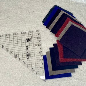 May include: A clear plastic quilting ruler with a grid pattern and the words "EASY ANGLE" printed on it. The ruler is 6 inches long and has markings in inches and fractions of an inch. There are 10 squares of fabric in various colors, including blue, gray, red, and black, arranged in a fan shape.