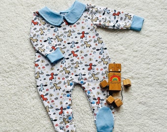 May include: A white baby onesie with a blue peter pan collar and a moose print. The onesie has blue accents on the cuffs and feet. The onesie is lying on a white fluffy surface.