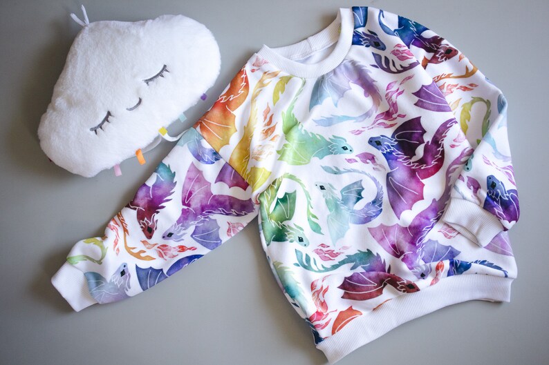 Puede incluir: Sudadera blanca con estampado de drag&oacute;n de acuarela arco&iacute;ris. Los dragones est&aacute;n volando y tienen llamas saliendo de sus bocas.