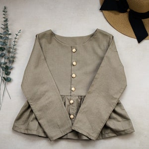 May include: A long-sleeved, light brown blouse with a ruffled hem and a row of gold buttons down the front.