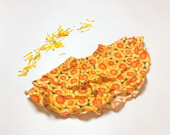 May include: A yellow and orange skirt with a sunflower print and multiple layers of ruffles.