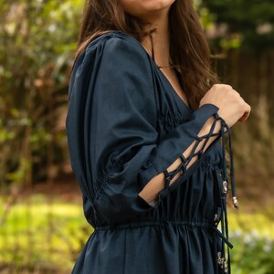 May include: A dark blue dress with long sleeves and a gathered waist. The sleeves have lace-up details and silver beads.
