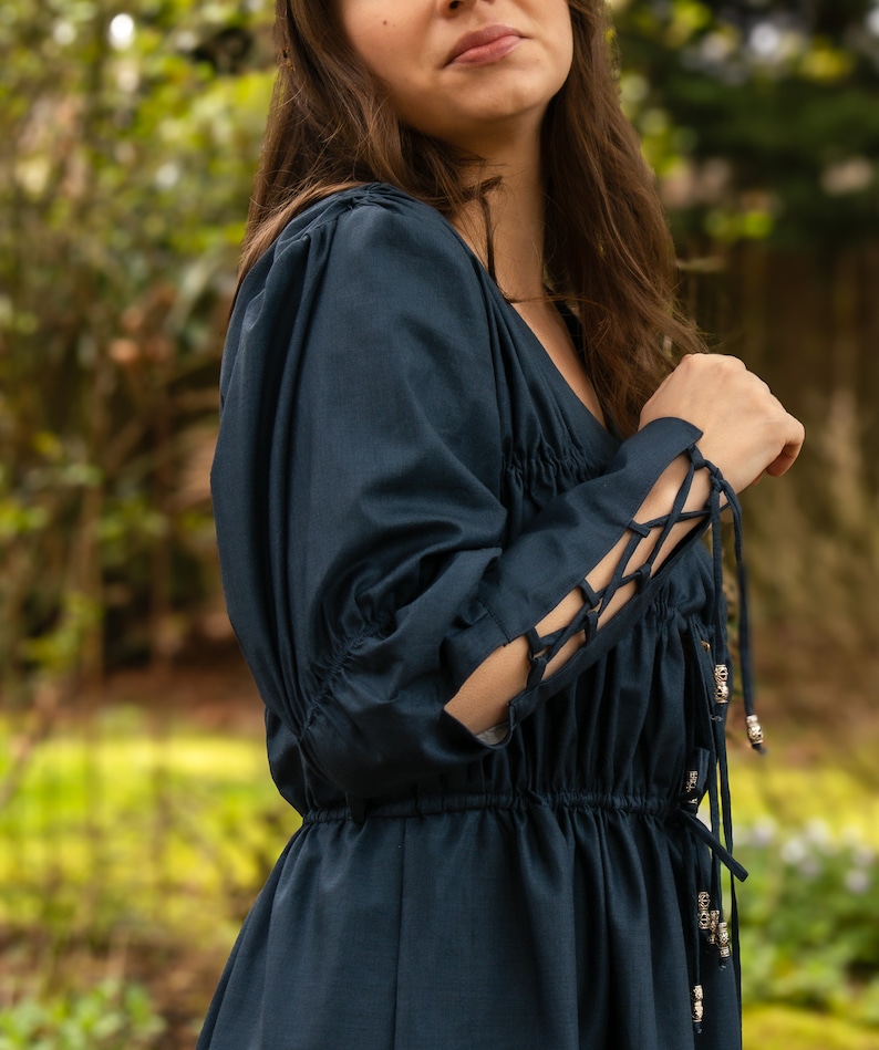 May include: A dark blue dress with long sleeves and a gathered waist. The sleeves have lace-up details and silver beads.