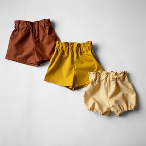Può includere: Tre paia di pantaloncini di diversi colori: marrone, giallo e beige. I pantaloncini sono realizzati in un tessuto morbido e leggero e hanno una vestibilità rilassata.