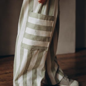 May include: Green and white striped pants with a large patch pocket on the left leg. The pants are made of a soft, lightweight fabric and have a relaxed fit.