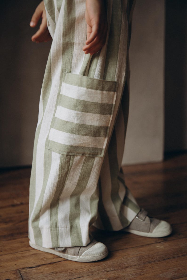 May include: Green and white striped pants with a large patch pocket on the left leg. The pants are made of a soft, lightweight fabric and have a relaxed fit.