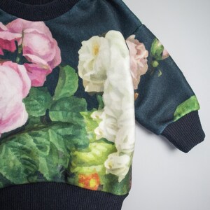Puede incluir: Una sudadera azul oscuro con estampado floral de rosas rosas, blancas y verdes. La sudadera tiene cuello y pu&ntilde;os de canal&eacute;.