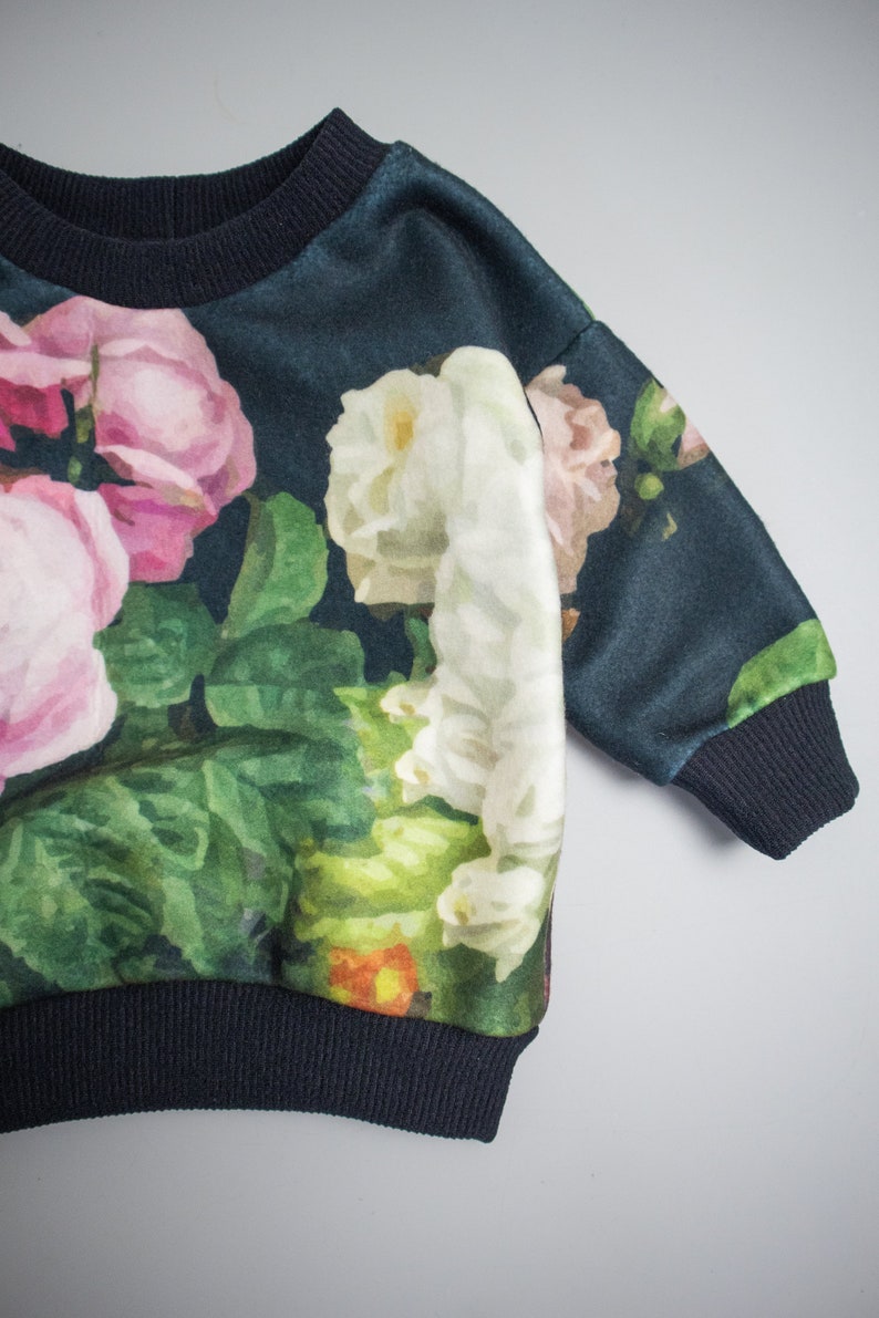 Puede incluir: Una sudadera azul oscuro con estampado floral de rosas rosas, blancas y verdes. La sudadera tiene cuello y pu&ntilde;os de canal&eacute;.