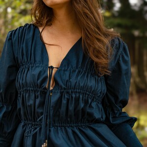 May include: A dark blue long-sleeved blouse with a gathered bodice and a tie at the neckline.
