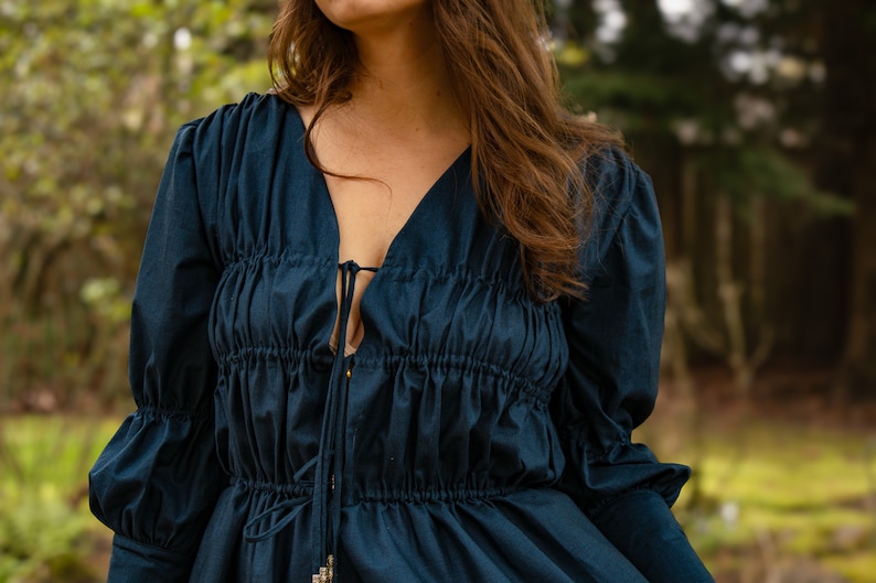 May include: A dark blue long-sleeved blouse with a gathered bodice and a tie at the neckline.