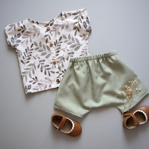 May include: A white and green leaf print short-sleeved shirt and green linen shorts with brown shoes.