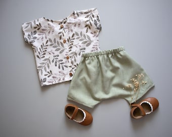 May include: A white and green leaf print short-sleeved shirt and green linen shorts with brown shoes.